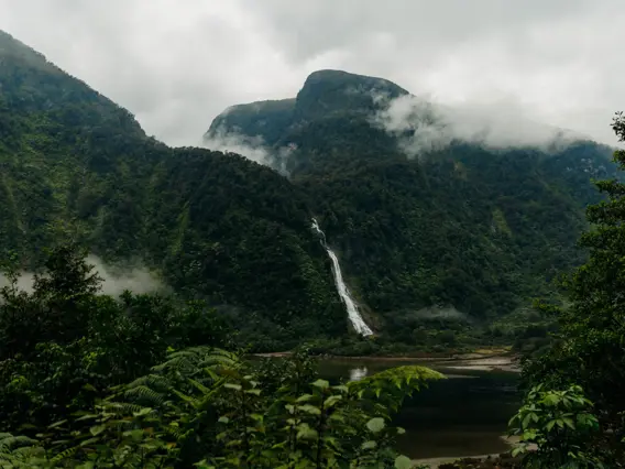 Mist-covered mountains and a waterfall rising above a remote fiord.