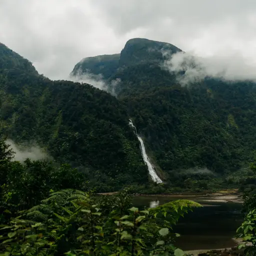 Mist-covered mountains and a waterfall rising above a remote fiord.