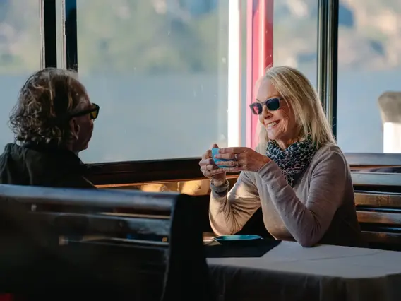 A coupld enjoy a cup of coffee seated indoors a cruise boat. 