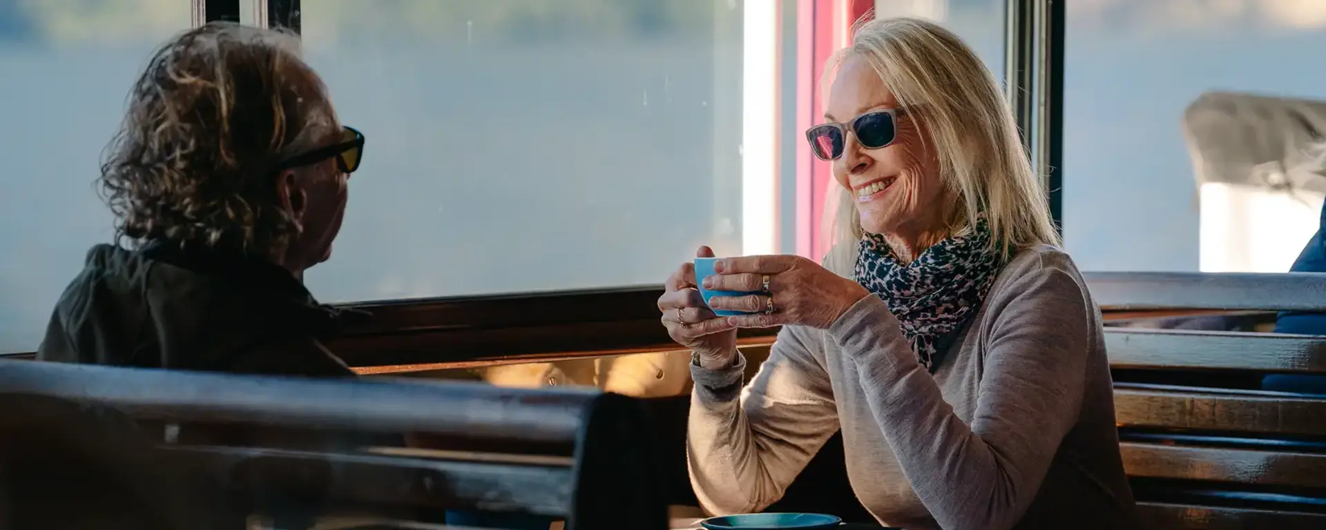 A coupld enjoy a cup of coffee seated indoors a cruise boat. 