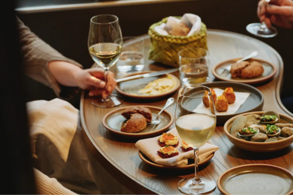 A cozy table setting with small plates of gourmet food and glasses of white wine.