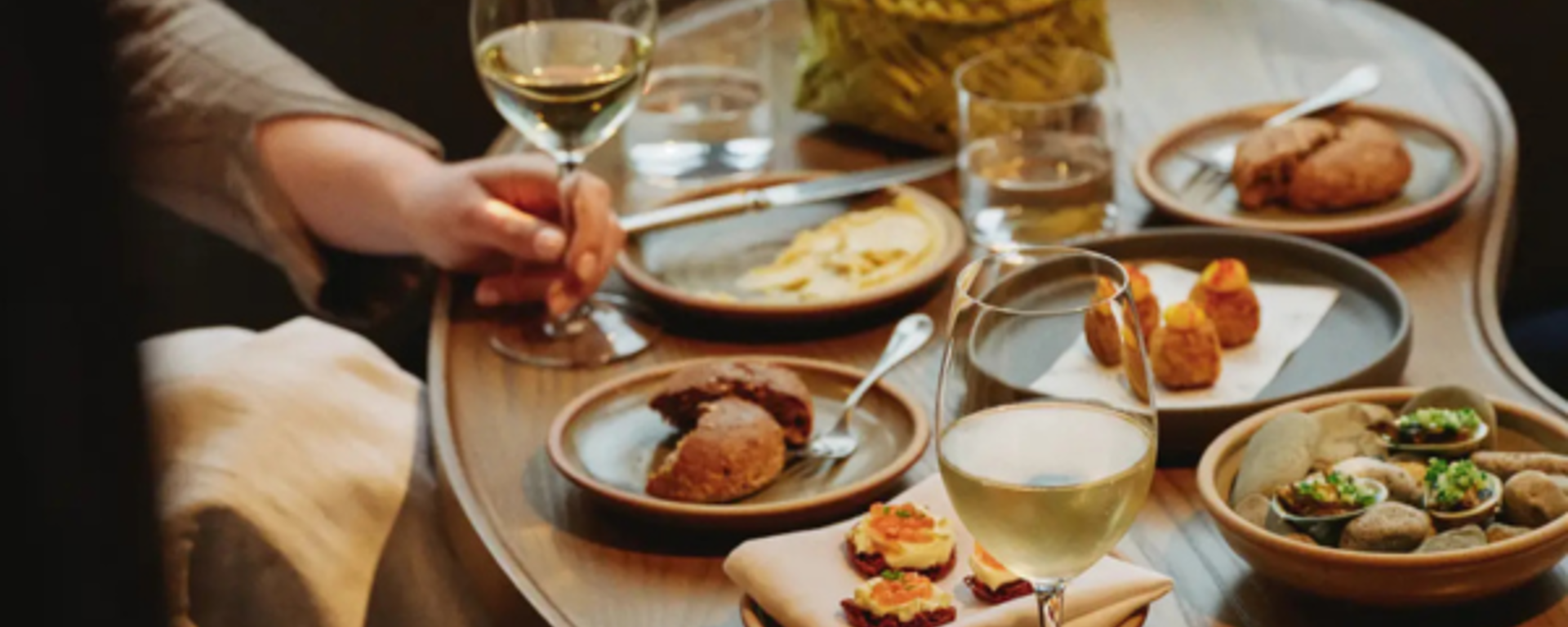 A cozy table setting with small plates of gourmet food and glasses of white wine.