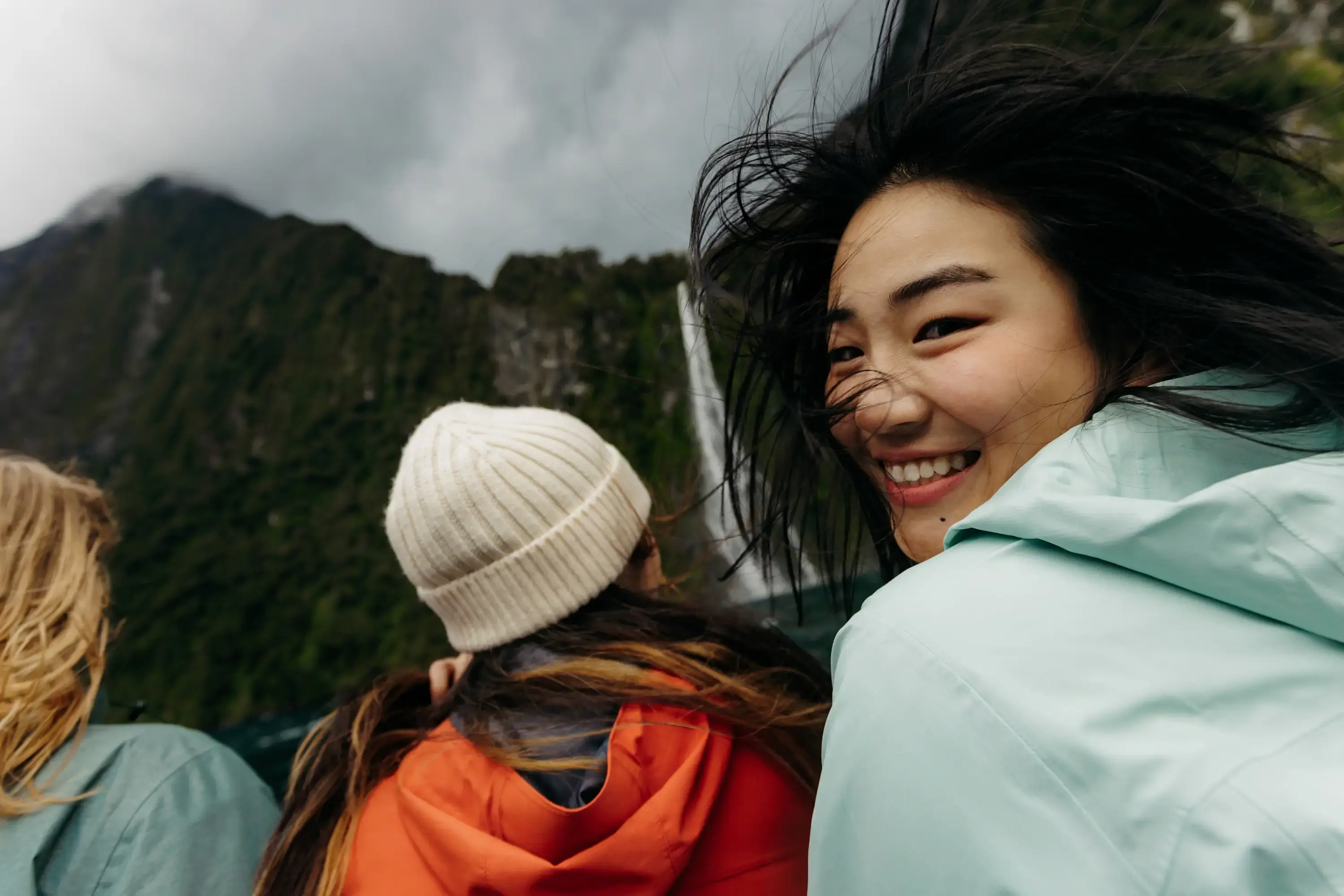 Smiling passenger enjoying a windy cruise beneath towering mountains.