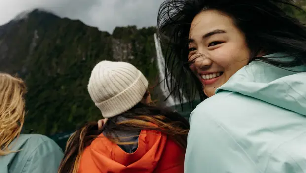 Smiling passenger enjoying a windy cruise beneath towering mountains.