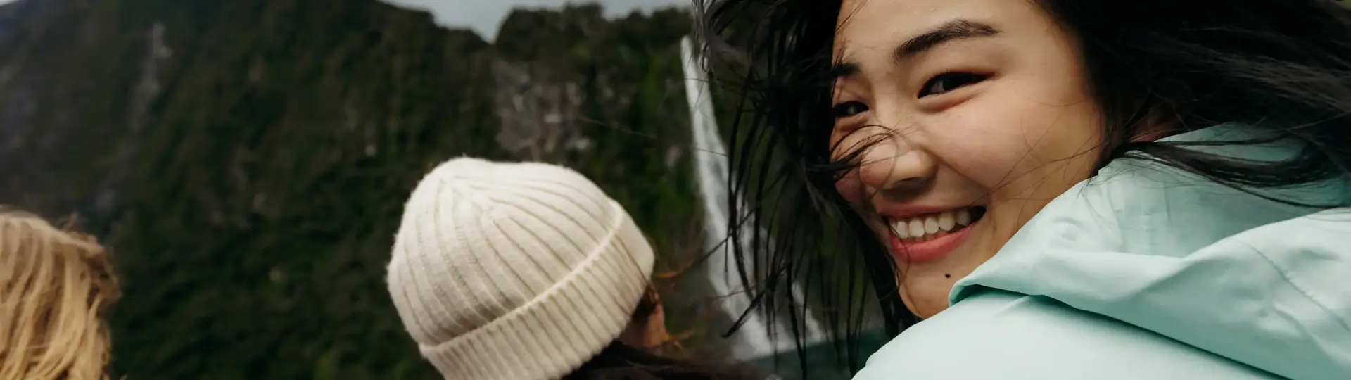Smiling passenger enjoying a windy cruise beneath towering mountains.