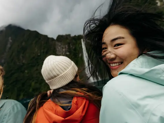 Smiling passenger enjoying a windy cruise beneath towering mountains.