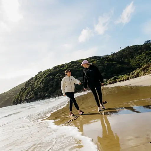 Two people walking along a sandy beach on Rakiura Stewart Island.