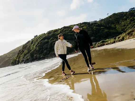 Two people walking along a sandy beach on Rakiura Stewart Island.