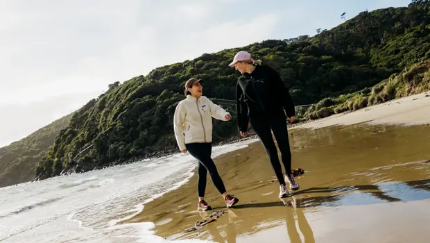 Two people walking along a sandy beach on Rakiura Stewart Island.