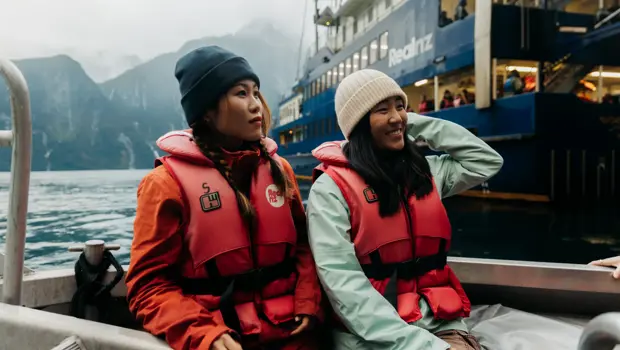Two women enjoy a tender boat ride, wearing RealNZ branded lifejackets.
