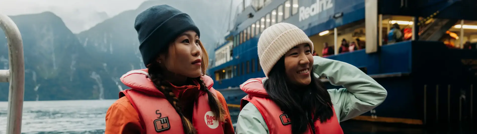 Two women enjoy a tender boat ride, wearing RealNZ branded lifejackets.
