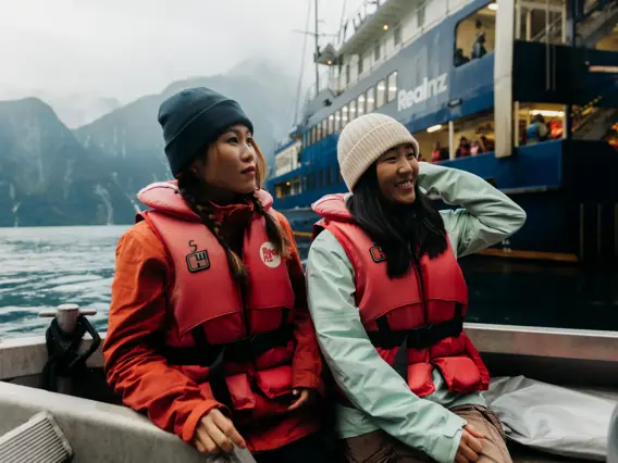 Two women enjoy a tender boat ride, wearing RealNZ branded lifejackets.