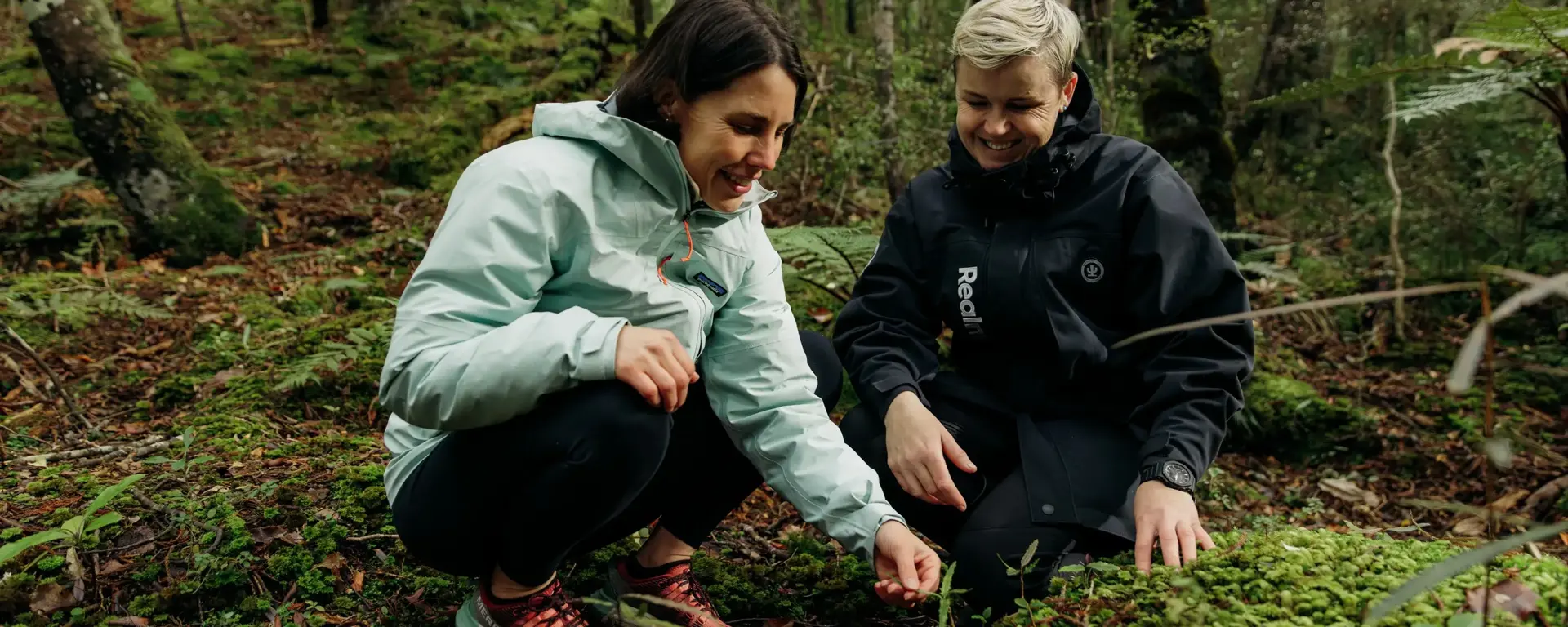 A guest and a guide explore plants on the native forest floor.