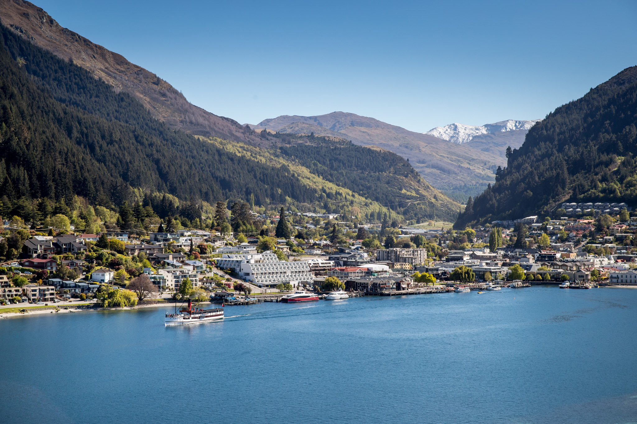 Drone view of the centre of Queenstown lakefront with with the famous TSS Earnslaw cruising on the lake and snow-capped mountains in the background.