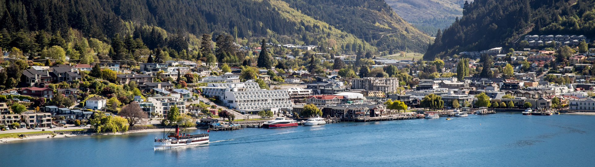 Drone view of the centre of Queenstown lakefront with with the famous TSS Earnslaw cruising on the lake and snow-capped mountains in the background.