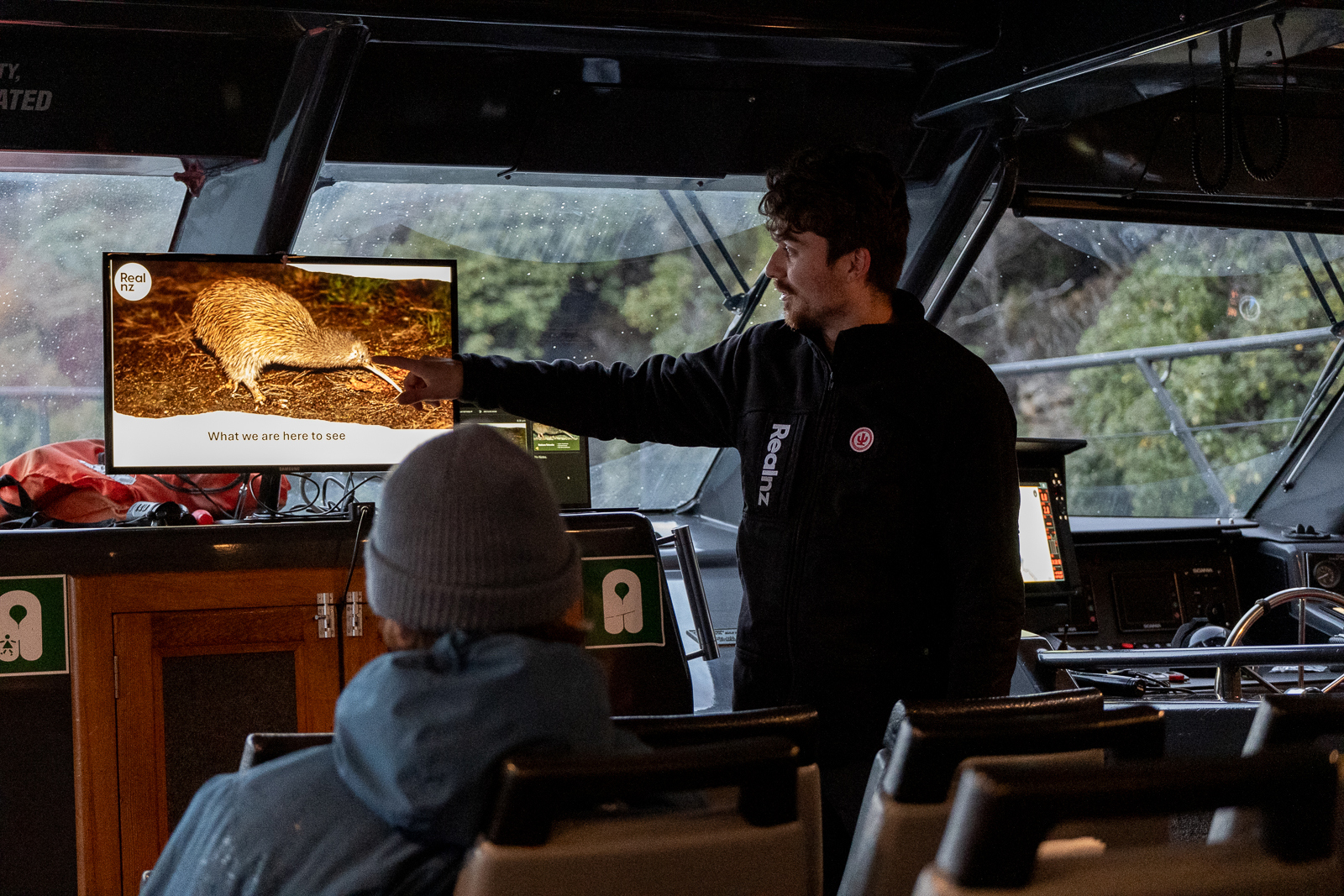 A RealNZ nature guide shows a presentation of wild kiwi on a cruise boat to guests.