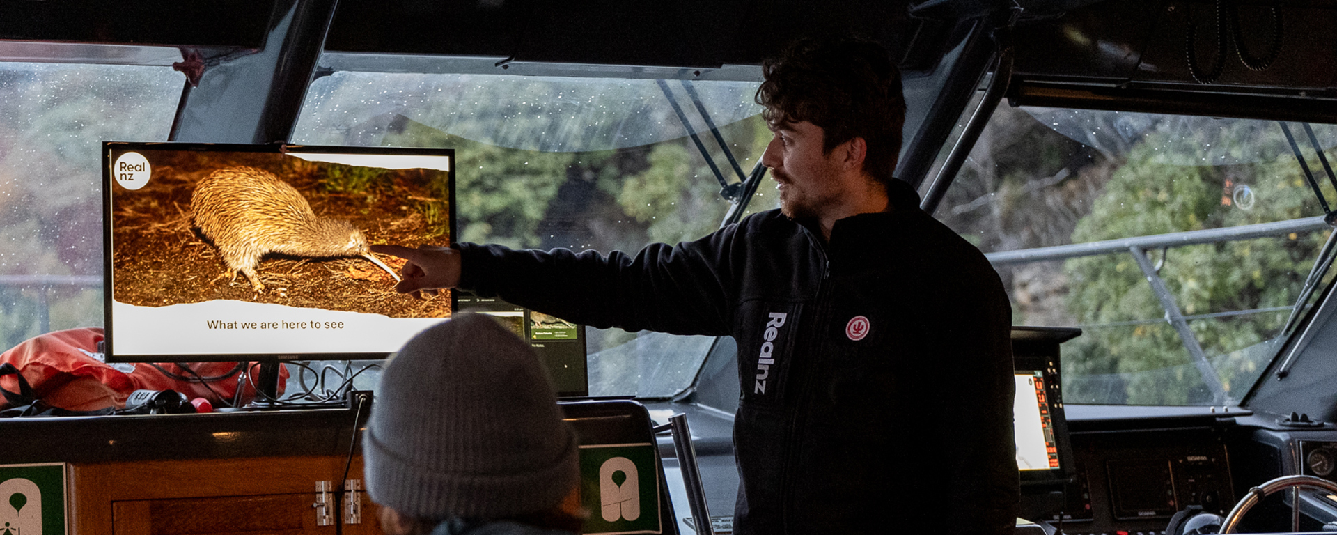 A RealNZ nature guide shows a presentation of wild kiwi on a cruise boat to guests.