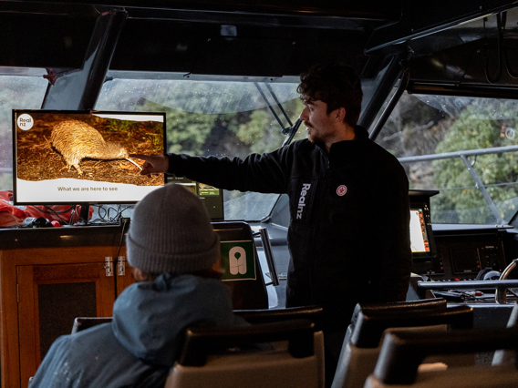 A RealNZ nature guide shows a presentation of wild kiwi on a cruise boat to guests.