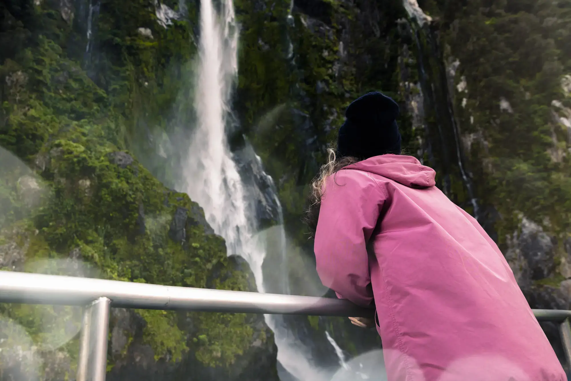 Guest in a pink jacket viewing a Milford Sound waterfall from the deck.