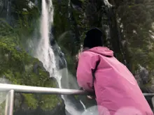 Guest in a pink jacket viewing a Milford Sound waterfall from the deck.